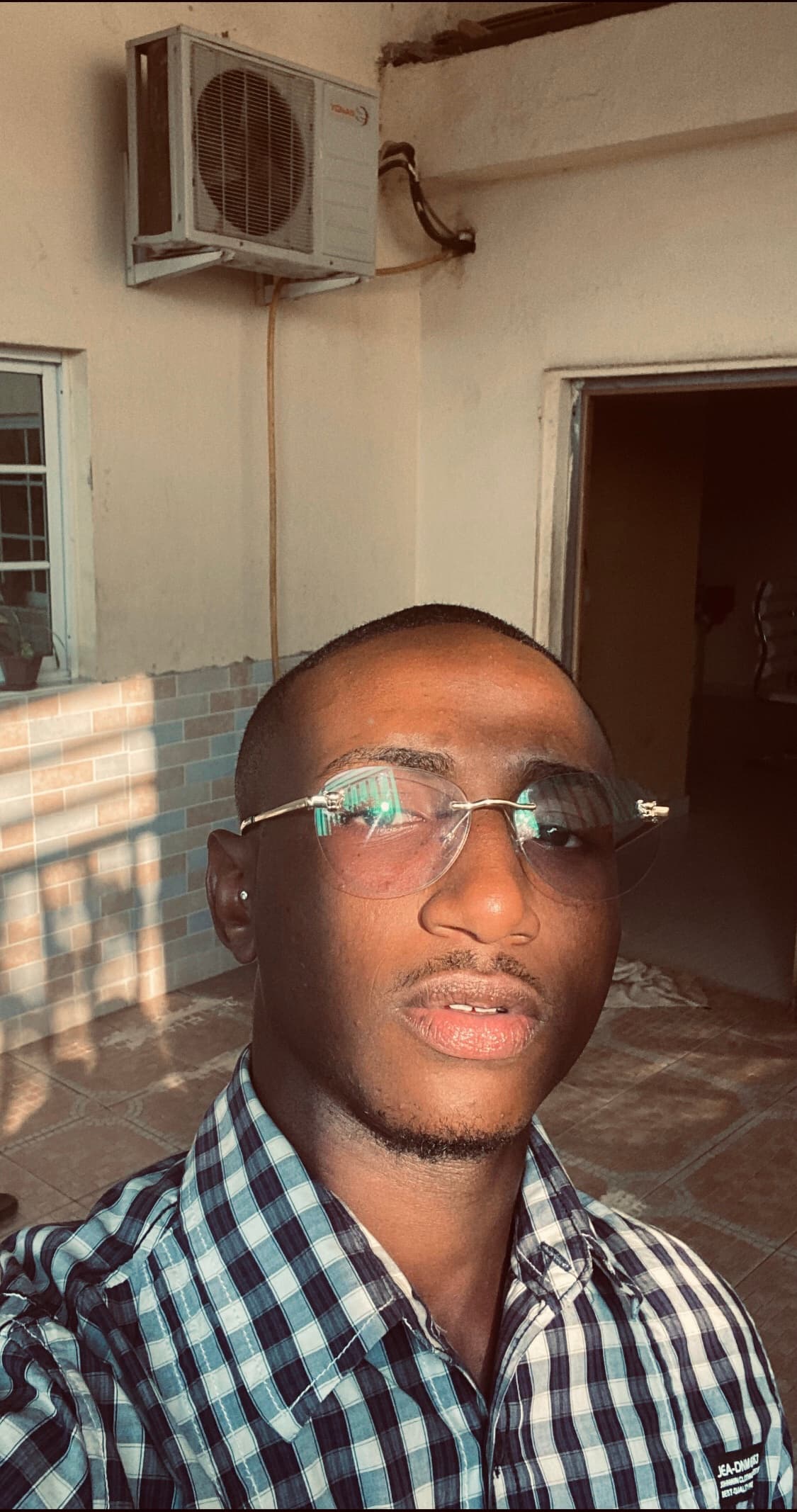 Young Black man in plaid shirt and sunglasses, sunlight reflecting on lenses, outdoor.